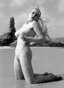 Margaret Nolan (Vicky Kennedy) kneeling in the shallows on a beach in Cornwall with the wind blowing her hair. A familiar spot for Harrison Marks to take his models, ca., 1964.